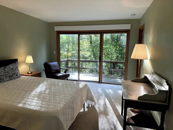 A bedroom with a large bed, a chair, a desk, and a view of a balcony with trees. - Guest House in the Trees w/ Pool & Tennis (New Milford)