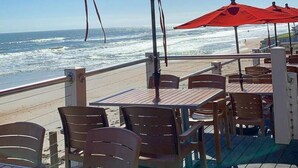 Ein Restaurant am Meer mit Terrassensitzgelegenheiten und roten Sonnenschirmen, mit Blick auf den Ozean.