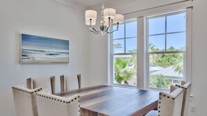 A dining area with a wooden table and upholstered chairs, a chandelier, and a large window with a view of greenery. - Sun Justice- 4 bd/4.5ba close to beach (Miramar Beach)