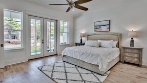 A bedroom with a bed, a ceiling fan, a nightstand, and a window with a view of greenery. - Sun Justice- 4 bd/4.5ba close to beach (Miramar Beach)