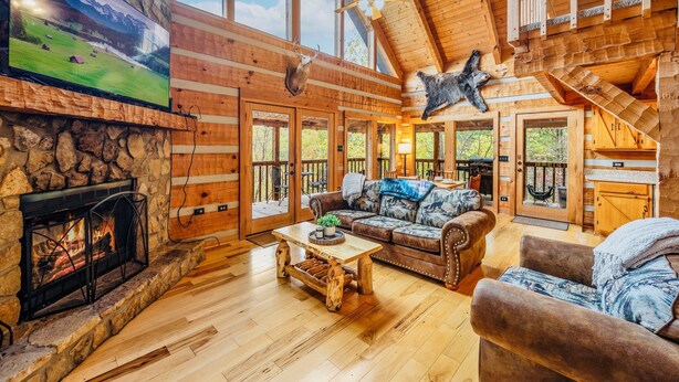 A log cabin interior with a stone fireplace, a large TV, and a cozy seating area. - Stairway to Heaven •Breathtaking Mountain Views• (Sevierville)