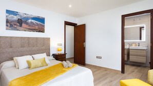 Habitación de hotel con cama, mesita de noche con lámpara, baño con espejo y suelo de madera.