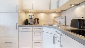 Eine moderne Küche mit weißen Schränken, einer Edelstahl-Kaffeemaschine, einem Wasserkocher, einem Toaster und einem Spülbecken.