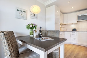 A modern kitchen with white cabinets, a built-in oven, and a dining area with a wooden table and wicker chairs.