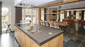 Una cocina moderna con una isla central, una zona de comedor con una mesa y sillas de madera, y una chimenea de piedra.