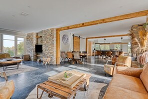 Un vaste espace de vie agrémenté d’une cheminée en pierre, un coin repas avec des chaises modernes et une grande fenêtre laissant entrer la lumière naturelle.