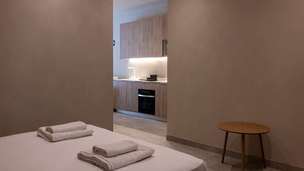 Ein Hotelzimmer mit Bett, zwei Handtüchern, einem kleinen runden Tisch und Blick in den Küchenbereich.