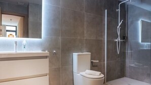 Uma casa de banho moderna com sanita, cabine de duche em vidro e toucador com espelho.