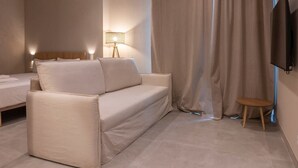 A modern hotel room with a sofa, a small table, a lamp, and a TV mounted on the wall. - VLC HOST - Palau A (Valencia)