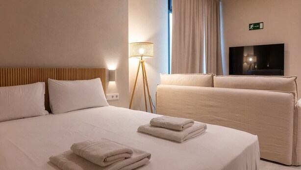 A hotel room with a large bed, a sofa, a floor lamp, and a TV. - VLC HOST - Palau A (Valencia)