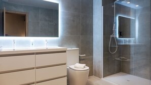 Ein modernes Badezimmer mit weißem Waschtisch, einer Duschkabine aus Glas und einer Toilette.