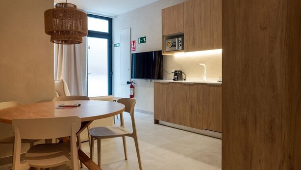 Eine moderne Küche mit Holzschränken, einer eingebauten Mikrowelle und einer Kaffeemaschine. Ein Essbereich mit rundem Tisch und Stühlen lädt zum Verweilen ein, und ein großes Fenster sorgt für natürliches Licht.