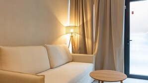 Ein modernes Hotelzimmer mit einer beigen Couch, einem kleinen Holztisch und einer Stehlampe.
