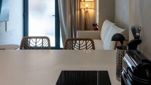 Una habitación de hotel moderna con un televisor de pantalla plana grande montado en la pared, una mesa de comedor con sillas, un purificador de aire negro TEKA y una ventana con cortinas.