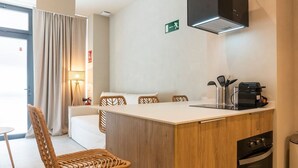 Habitación de hotel pequeña con kitchenette, zona de comedor con una mesa y sillas, cama y ventana con cortinas.