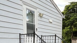 Une maison avec un escalier en béton menant à une porte, une boîte aux lettres et une poubelle verte.