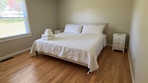 Une chambre avec un grand lit, une table de chevet, une fenêtre avec des stores et un luminaire au plafond.