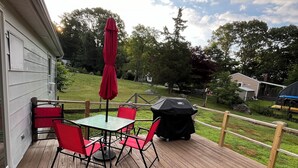 Une terrasse en bois avec une table et des chaises, un parasol rouge et un barbecue.