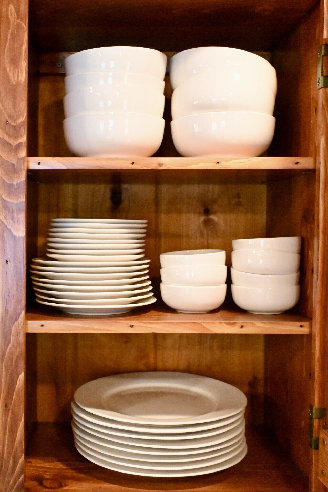 Un armario de madera con repisas que contienen cuencos y platos blancos.