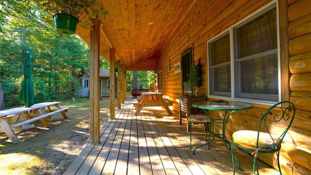 Eine Holzhütte mit einer Veranda, Picknicktischen und Sitzgelegenheiten im Freien.