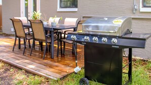 Une terrasse extérieure équipée d’un barbecue, d’une table à manger, de chaises et d’une plante en pot.