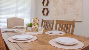 Une table de salle à manger en bois, dressée avec de l’argenterie blanche, des sets de table et un centre de table composé de coquillages et de fleurs.