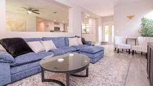 Un salon moderne avec un canapé d’angle bleu, une table basse en verre et un tapis à motifs.