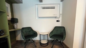 A small room with two green chairs, a small round table, a white air conditioning unit, and a lamp on a shelf. - Room/private bathroom in centre (Amsterdam)
