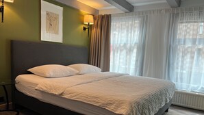 A neatly made bed with white linens in a room with green walls, a framed artwork, and a window with sheer curtains. - Room/private bathroom in centre (Amsterdam)