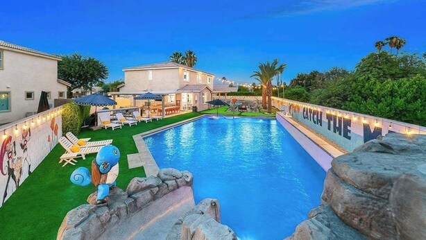 A swimming pool with lounge chairs and umbrellas, surrounded by buildings and greenery. - Catch The Magic- Pokémon Slide, Arcade, Pickleball (Indio)