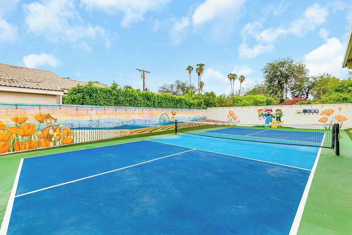 Una cancha de tenis al aire libre con un mural colorido en las paredes circundantes.