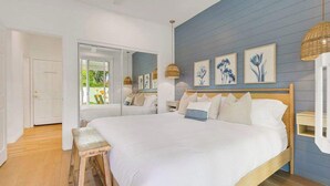 A bedroom with a large bed, a wooden bench, a door labeled 'Game Room,' and wall-mounted artwork. - Catch The Magic- Pokémon Slide, Arcade, Pickleball (Indio)