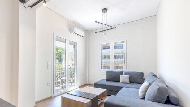Ein modernes Wohnzimmer mit einem grauen Sofa, einem Holztisch und einer Deckenleuchte.