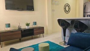 A living room with a flat-screen TV, a wooden cabinet, a blue sofa, and a kitchen area with a refrigerator. - Condo in Gros Islet 10 mins drive to beach (Gros Islet)