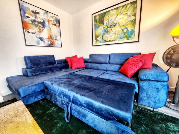 A blue sectional sofa with red cushions, a black floor lamp, and abstract paintings on the walls.