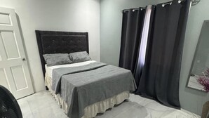 A bedroom with a bed, curtains, a fan, and a mirror.