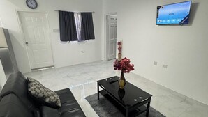 A living room with a black leather sofa, a coffee table with a vase of flowers, a flat-screen TV on the wall, and a door with a black curtain.