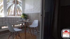 A balcony with a table and chairs, a potted plant, and a view of palm trees.