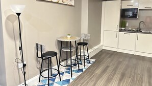 A modern kitchen with white cabinets, a built-in microwave, and a small dining area with a round table and two bar stools. - 2 Bed Apartment - Sleeps 4 - Wifi - Parking (Dudley)
