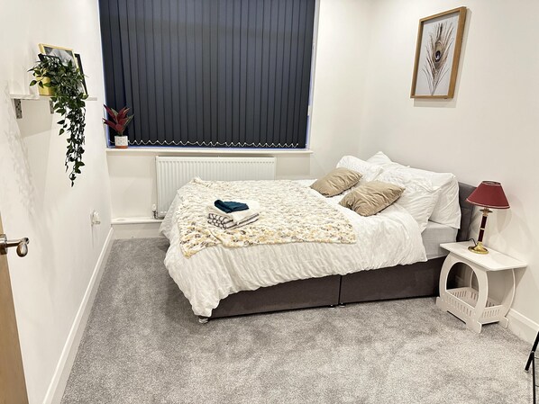 Une chambre à coucher avec un lit, une table de chevet, une lampe et une fenêtre avec des stores.
