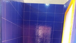 A small bathroom with blue tiles, a white toilet, and a yellow and blue striped shower curtain.