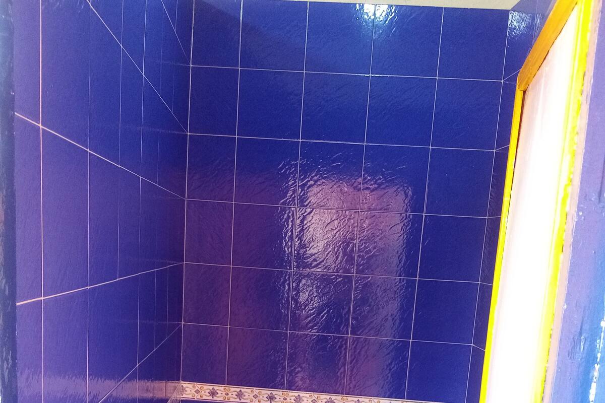 Une petite salle de bain avec des carreaux bleus, des toilettes blanches et un rideau de douche à rayures jaunes et bleues.