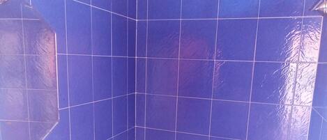 A bathroom with blue tiles, a white sink, and a shower with a white hose.