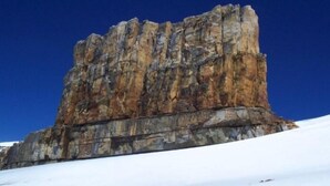 A large rock formation with a flat top, surrounded by snow.