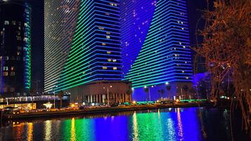 A nighttime view of two illuminated skyscrapers with reflections on a body of water.