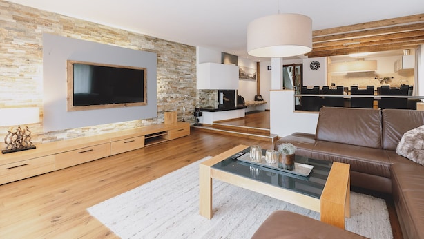 Ein modernes Wohnzimmer mit Flachbildfernseher, Holzboden, einem Glastisch und einem Ledersofa.
