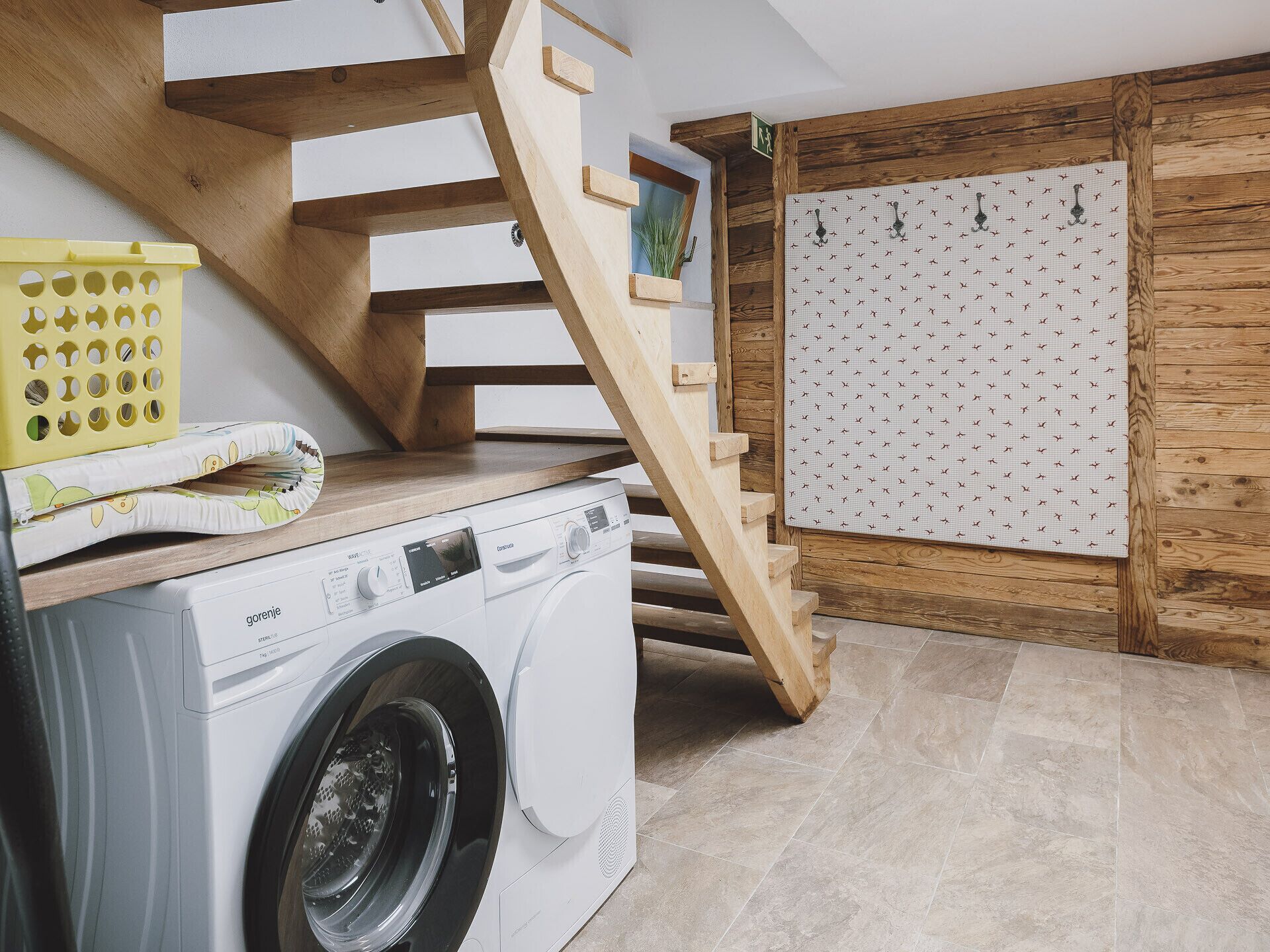 A laundry area with a washing machine, wooden stairs, and a patterned wall.