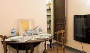 A dining area with a wooden table set for two, featuring blue and white ceramic dishes, a framed artwork, and a television mounted on the wall. - Michelangelo's Refuge. Ponte Vecchio, Florence. (Firenze)