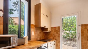 Cocina compacta con microondas, estufa y horno, armarios de madera y vistas a zonas verdes a través de una puerta.