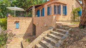 Un edificio rústico de piedra con una escalera que lleva a una puerta, rodeado de árboles y follaje.